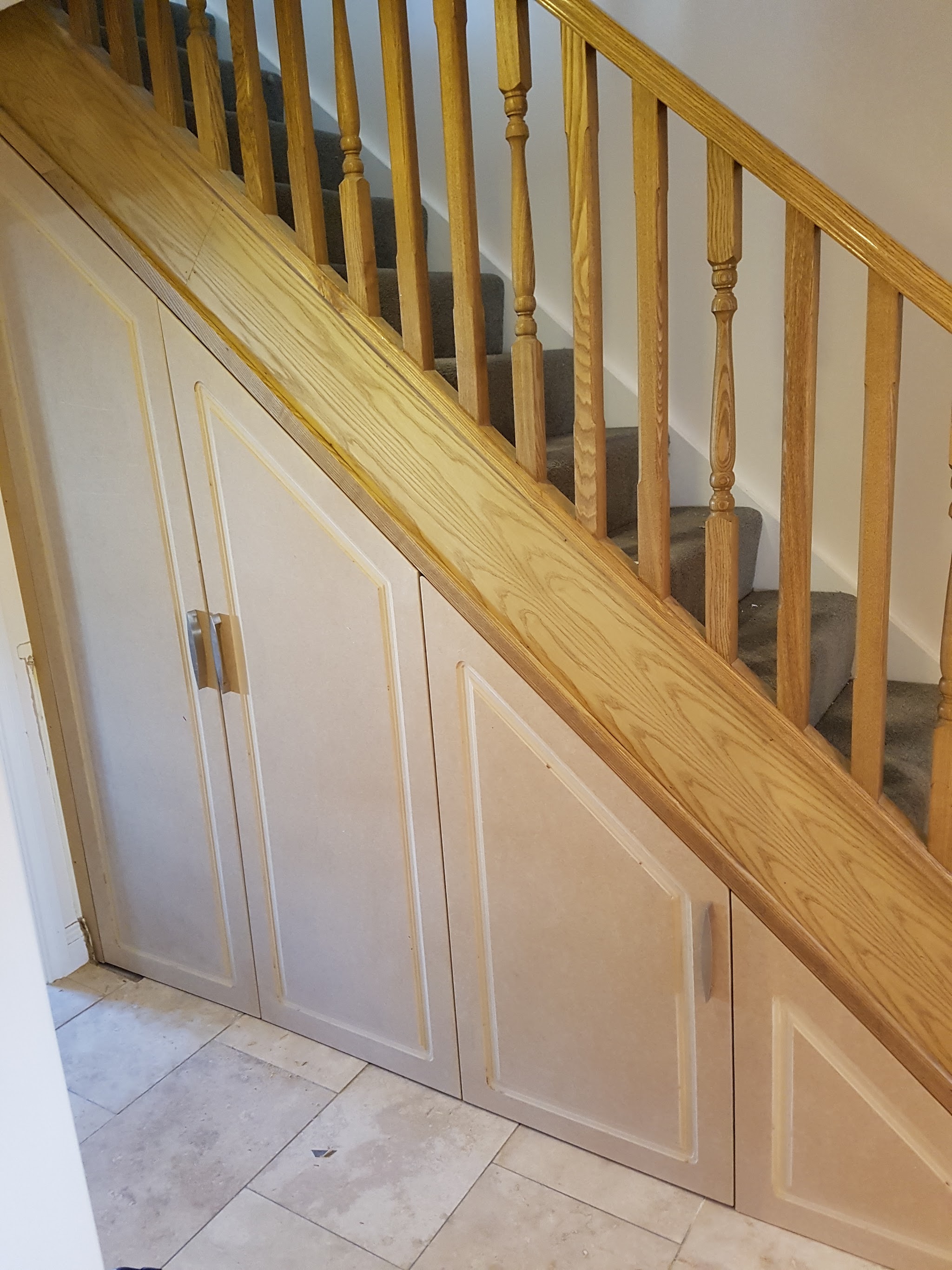 Panelled cupboards built into the full length of the space under an oak staircase