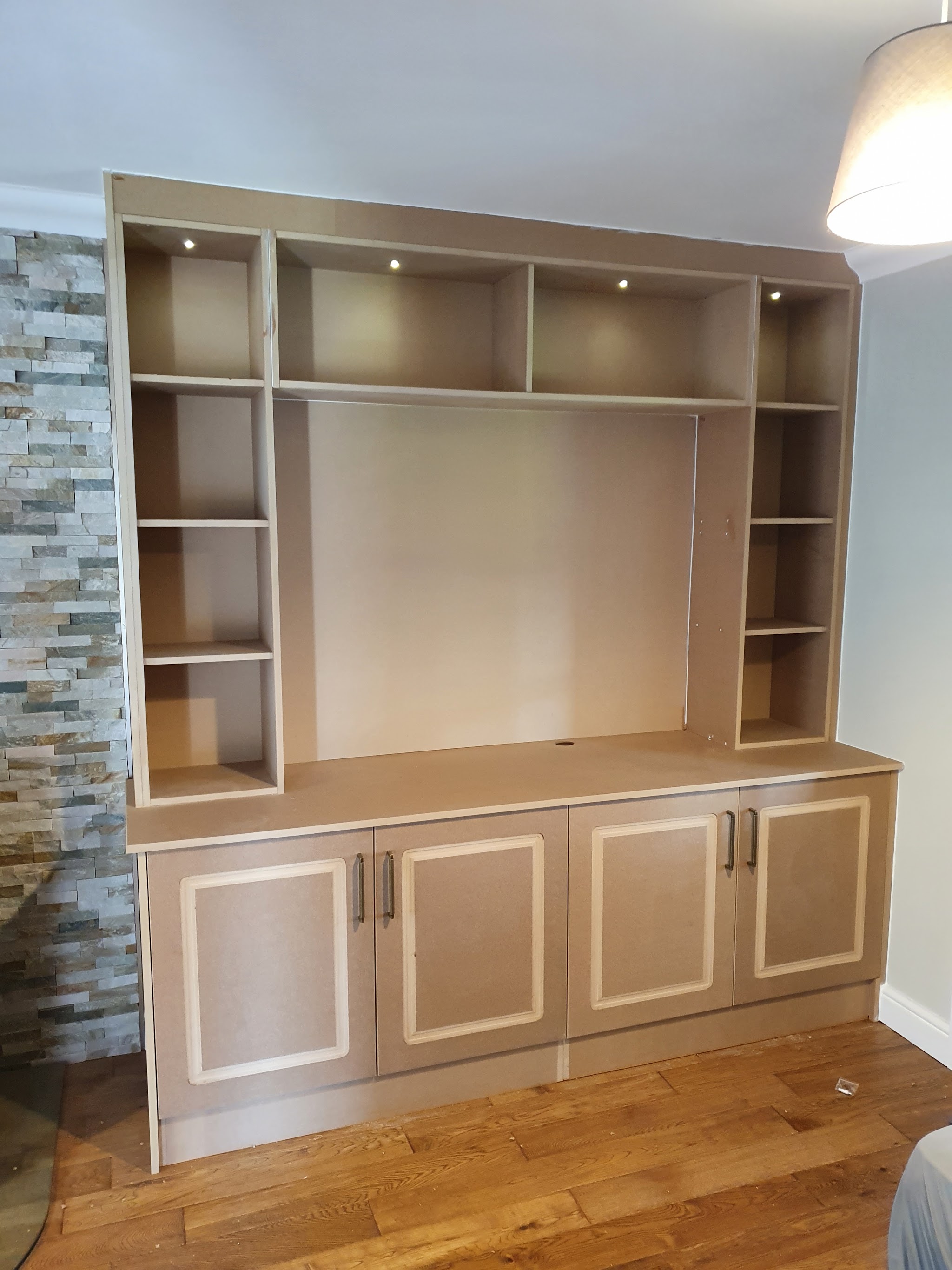 A large fitted shelving unit with cupboards below and downlights in the top shelves