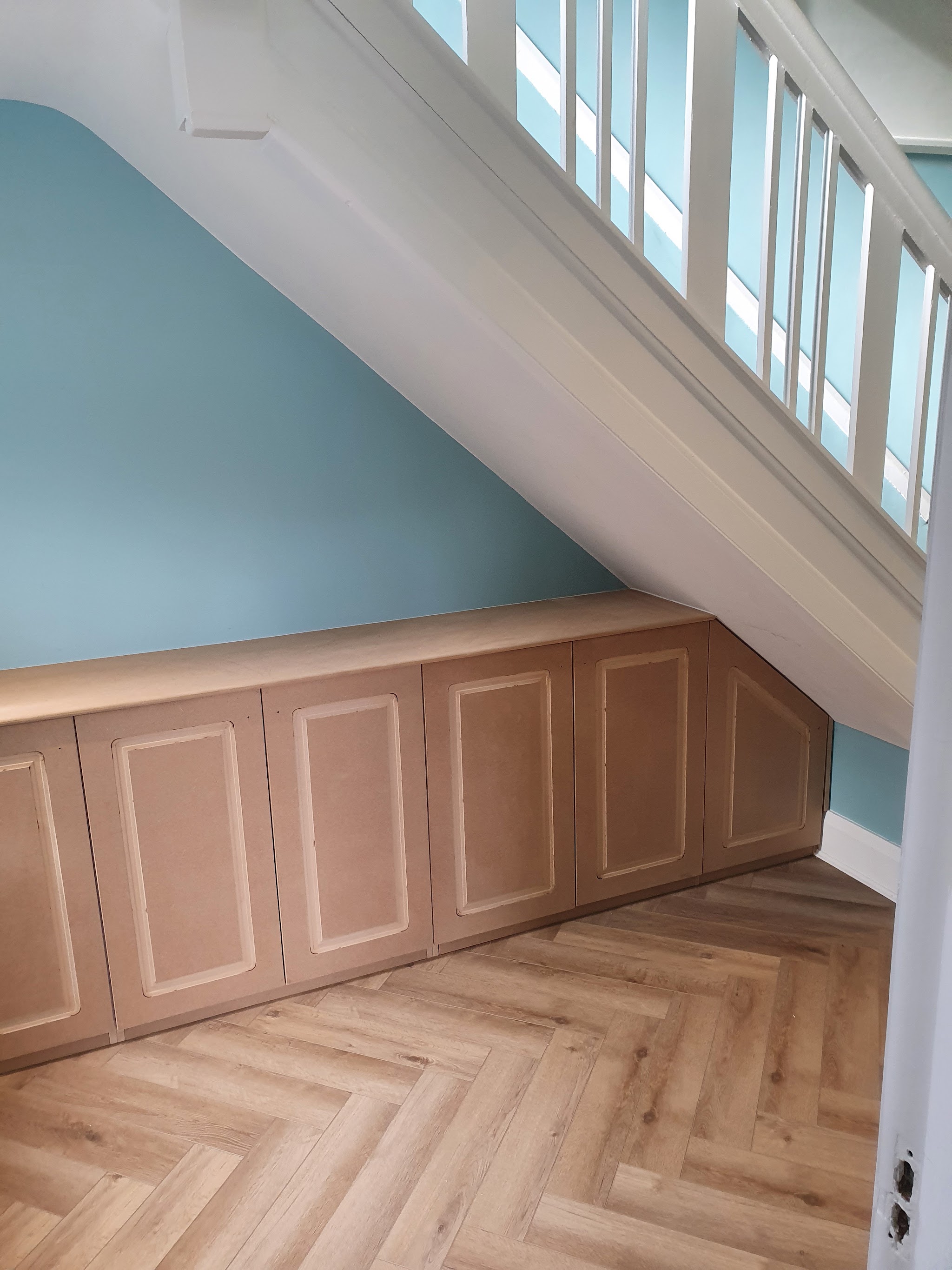 A long run of panelled under-stair cupboards in bare MDF above a herringbone floor