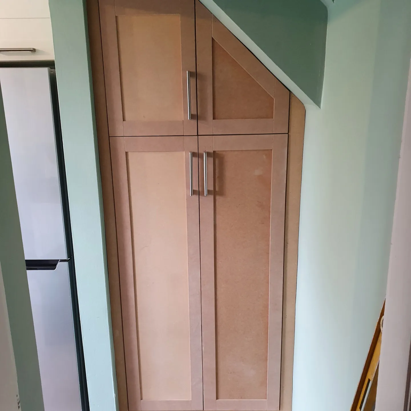 A tall shaker-style cupboard built into a stairway alcove